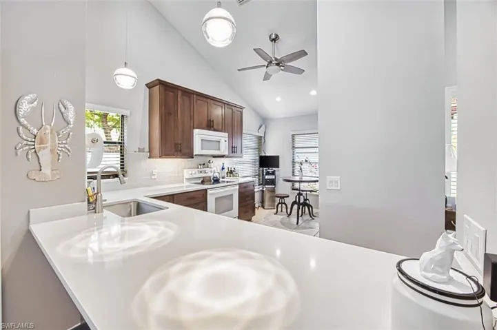 Kitchen featuring white appliances, vaulted ceiling, pendant lighting, a ceiling fan, and decorative backsplash