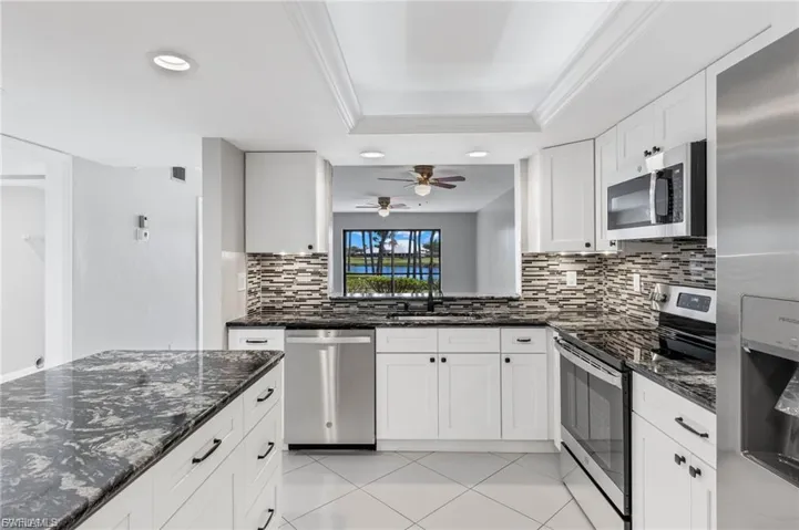 Kitchen featuring stainless steel appliances, dark stone counters, white cabinetry, recessed lighting, and light tile patterned floors