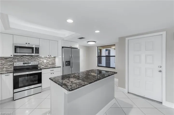 Kitchen featuring appliances with stainless steel finishes, white cabinetry, dark stone counters, recessed lighting, and a center island