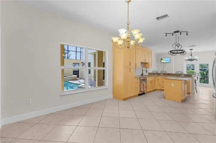 Eat-in kitchen featuring pendant lighting, light brown cabinetry, kitchen peninsula, and a notable chandelier