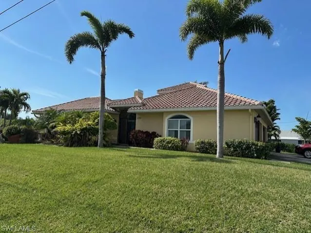 View of front facade featuring a front lawn and mature, tropical landscaping