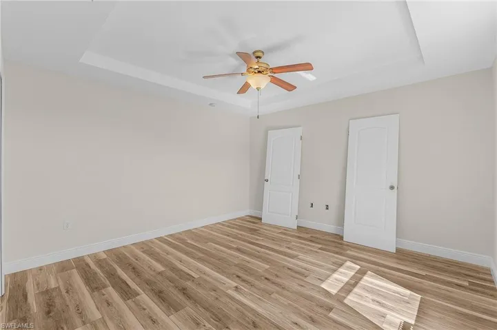 Guest bedroom with light vinyl plank floors, a raised ceiling, and ceiling fan