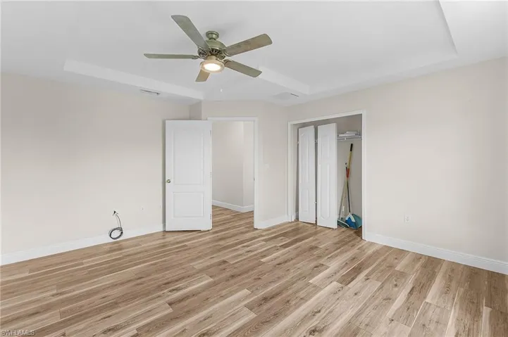 Guest bedroom with ceiling fan, a raised ceiling, a closet, and light vinyl plank flooring
