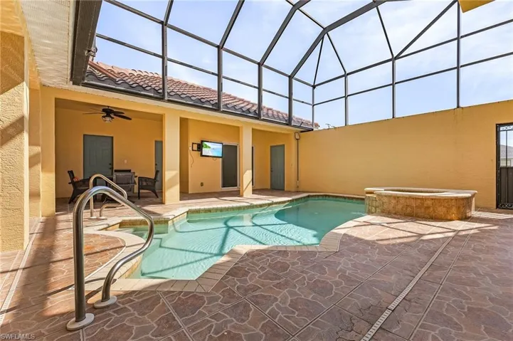 View of pool with ceiling fan, a patio area, glass enclosure, and a spillover spa!