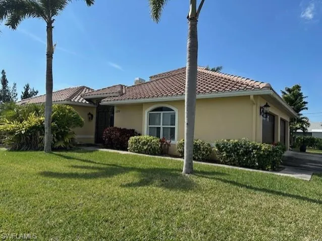 View of front of property featuring a front lawn and lush, tropical landscaping