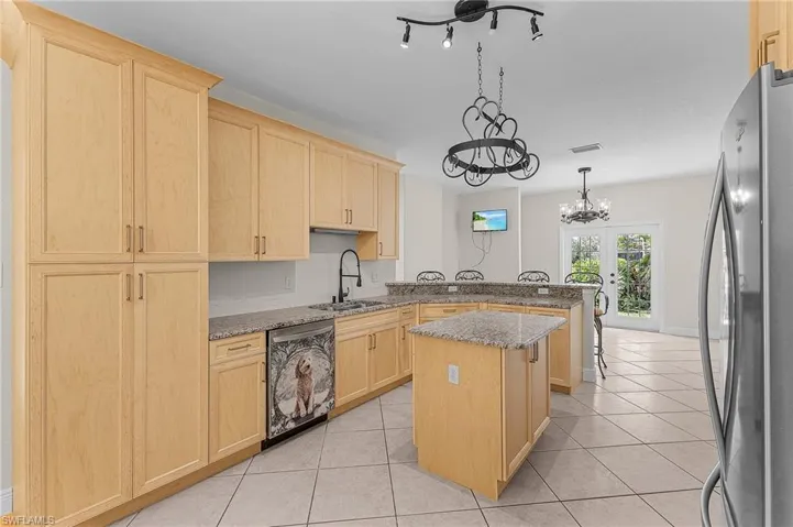 Kitchen with sink, appliances with stainless steel finishes, a center island, light stone counters, and light brown cabinetry