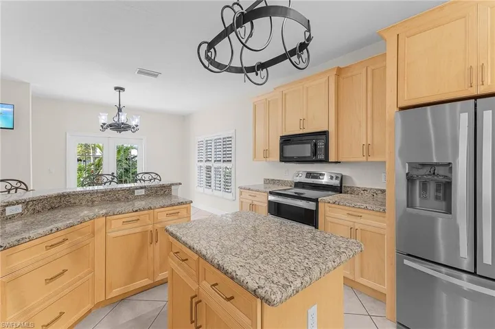 Kitchen featuring a chandelier, stainless steel appliances, light brown cabinetry, and a center island