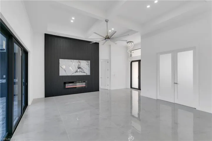 Empty room featuring a high ceiling, a premium fireplace, ceiling fan, and beamed ceiling