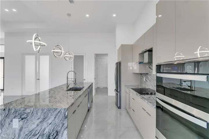 Kitchen featuring light stone counters, pendant lighting, stainless steel appliances, gray cabinetry, and sink