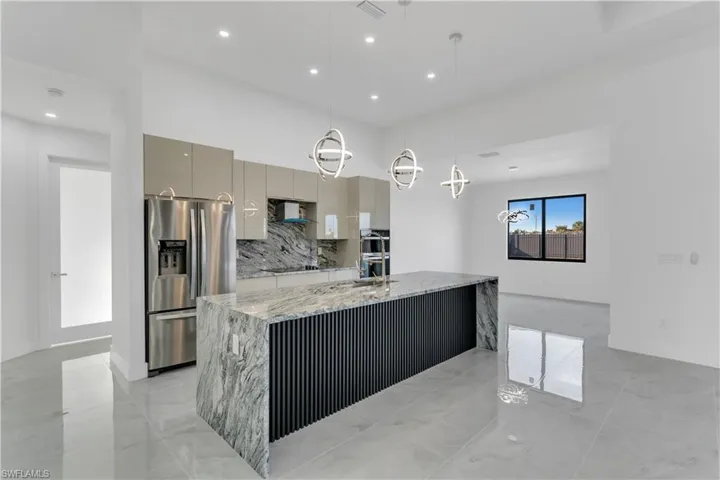 Kitchen featuring light stone counters, backsplash, hanging light fixtures, stainless steel refrigerator with ice dispenser, and gray cabinetry