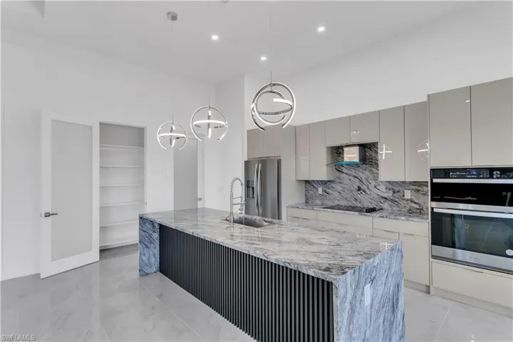 Kitchen with backsplash, hanging light fixtures, gray cabinets, a center island with sink, and appliances with stainless steel finishes