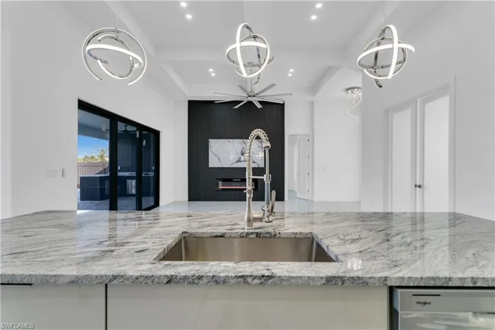 Kitchen featuring sink, a fireplace, light stone counters, ceiling fan, and stainless steel dishwasher