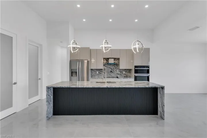Kitchen with light stone counters, stainless steel fridge with ice dispenser, gray cabinets, backsplash, and sink