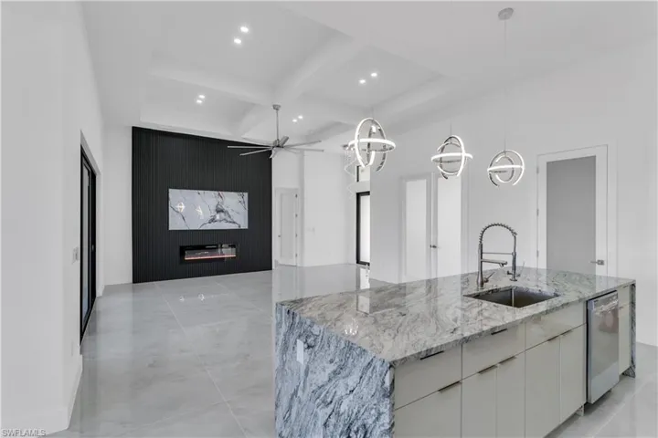 Kitchen featuring light stone counters, hanging light fixtures, a center island with sink, white cabinets, and sink