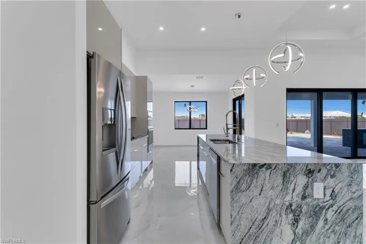 Kitchen with sink, light stone counters, a large island with sink, hanging light fixtures, and appliances with stainless steel finishes