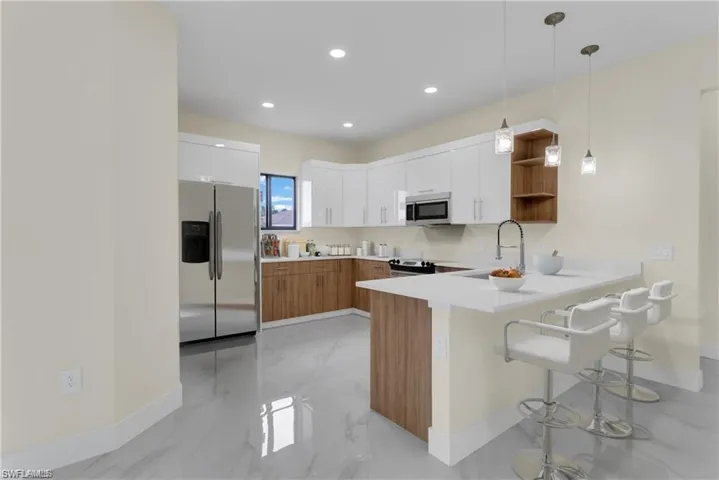 Kitchen with white cabinetry, sink, kitchen peninsula, decorative light fixtures, and appliances with stainless steel finishes