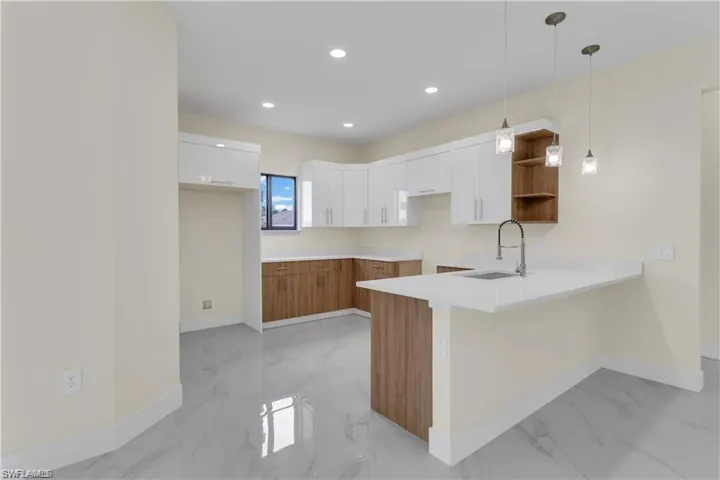 Kitchen featuring kitchen peninsula, sink, white cabinets, and decorative light fixtures