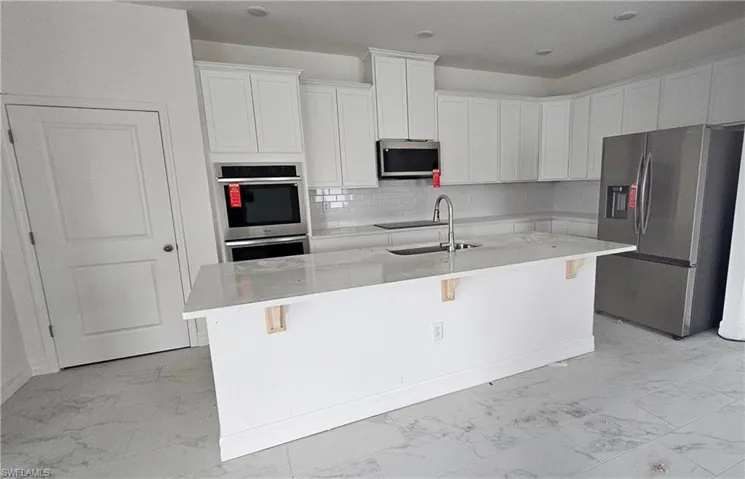 Kitchen featuring a breakfast bar area, a center island with sink, white cabinets, and stainless steel appliances