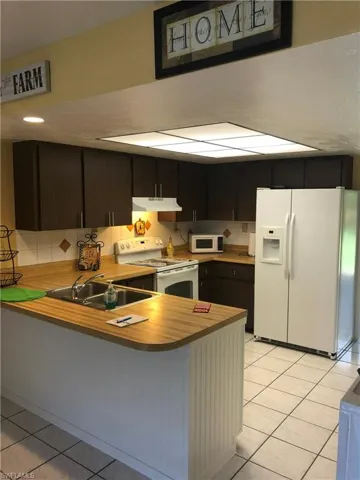Kitchen with white appliances, light tile patterned floors, a peninsula, and light countertops