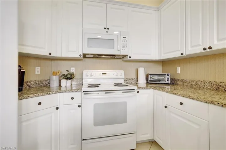 Kitchen featuring white appliances, light tile patterned floors, light stone counters, and white cabinetry