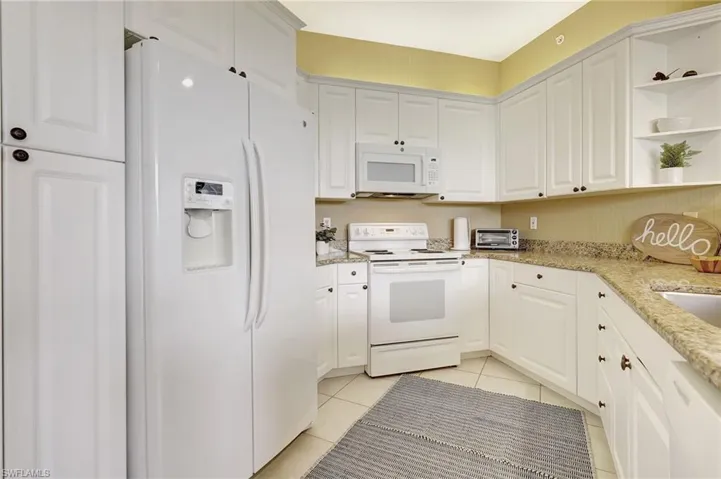 Kitchen featuring white appliances, white cabinets, light stone countertops, and light tile patterned floors