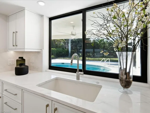 Kitchen with a sink, light stone countertops, ceiling fan, and white cabinetry