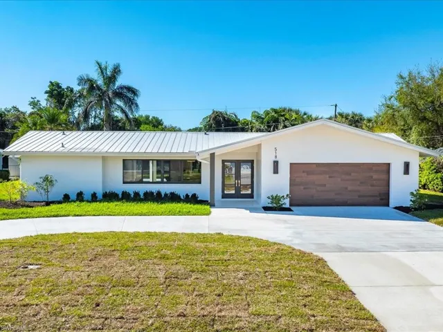View of front facade with a front yard, an attached garage, stucco siding, concrete driveway, and french doors