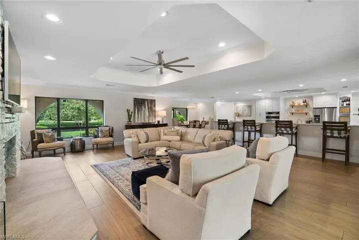 Living room with a raised ceiling, ceiling fan, a stone fireplace, and light hardwood / wood-style floors