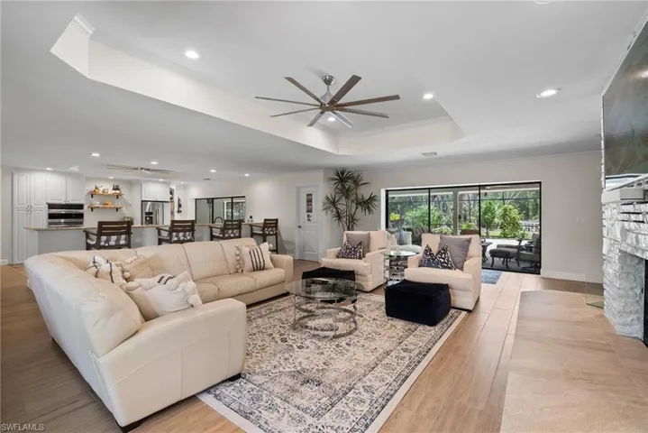 Living room featuring a tray ceiling, light wood-type flooring, ceiling fan, and a stone fireplace