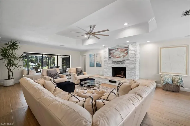 Living room featuring a raised ceiling, ceiling fan, light wood-type flooring, and a fireplace
