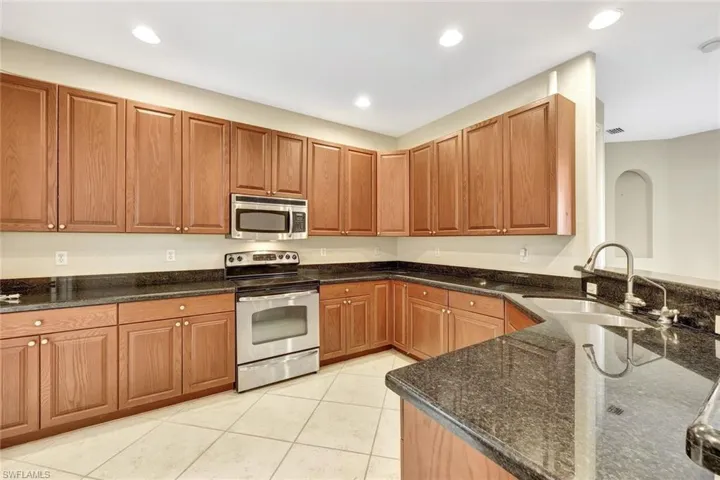 Kitchen featuring recessed lighting, dark stone countertops, a sink, light tile patterned flooring, and appliances with stainless steel finishes