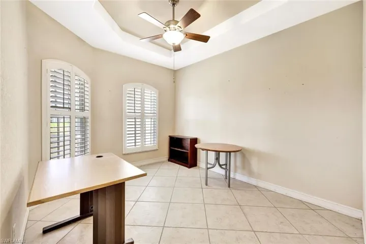 Office area with a ceiling fan, light tile patterned floors, a tray ceiling, and baseboards