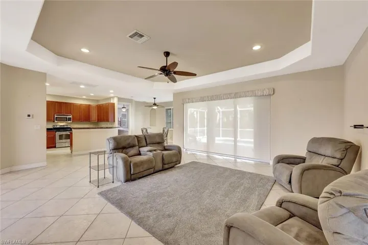 Living room with a ceiling fan, a raised ceiling, light tile patterned floors, and visible vents