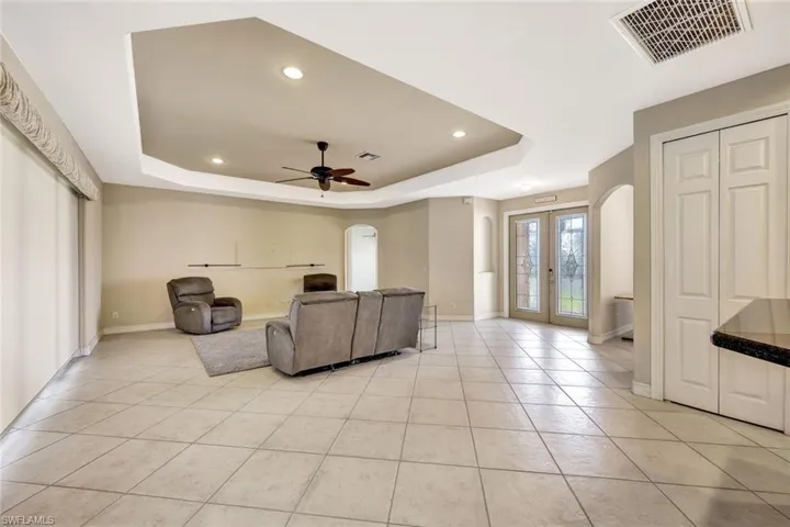 Living area with light tile patterned floors, arched walkways, a tray ceiling, and visible vents