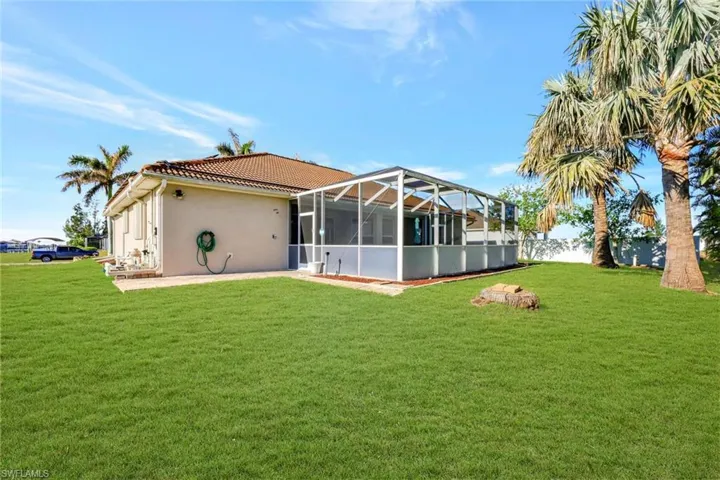 Rear view of house featuring a tile roof, a lanai, stucco siding, and a lawn