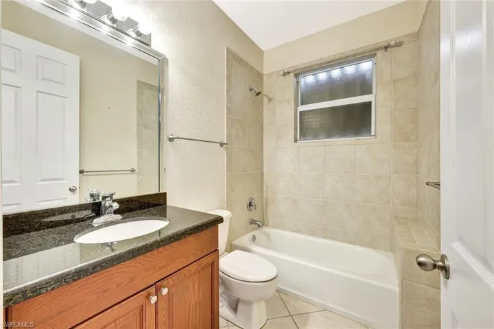 Full bathroom with toilet, vanity, shower / washtub combination, a textured wall, and tile patterned flooring