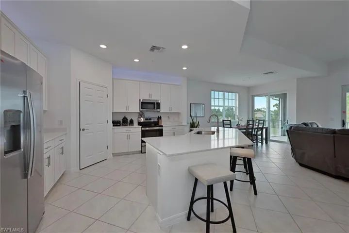 Kitchen with stainless steel appliances, white cabinetry, recessed lighting, light tile patterned flooring, and an island with sink. Additional dining space not pictured.
