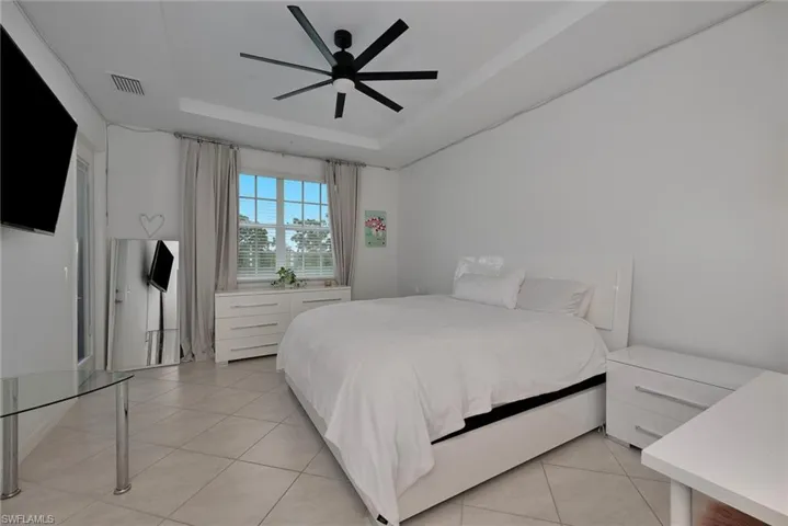 Bedroom with light tile patterned flooring, a tray ceiling, and a ceiling fan