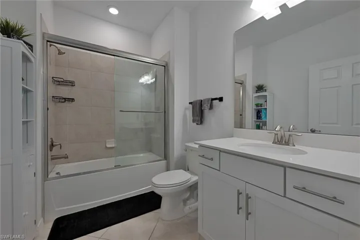 Bathroom with bath / shower combo with glass door, vanity, and light tile patterned floors