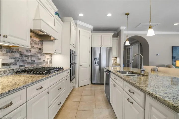 Kitchen featuring appliances with stainless steel finishes, pendant lighting, white cabinetry, sink, and custom range hood