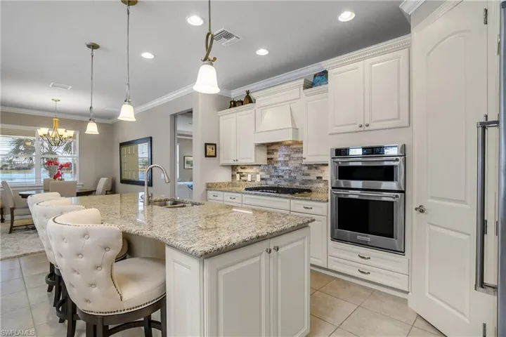 Kitchen featuring double oven, decorative light fixtures, sink, light stone counters, and a center island with sink