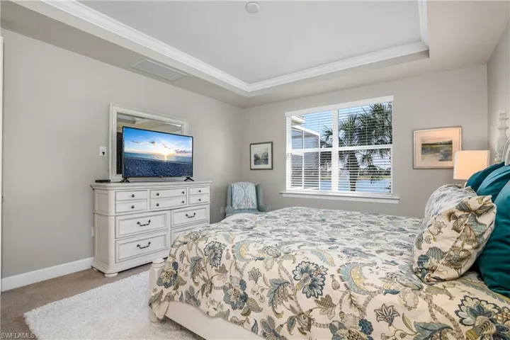 Bedroom featuring a raised ceiling, crown molding, and light carpet