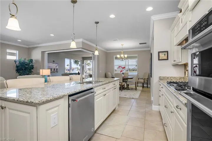 Kitchen with white cabinetry, crown molding, decorative light fixtures, appliances with stainless steel finishes, and a kitchen island with sink