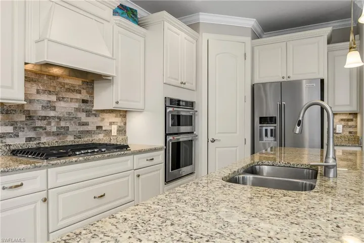 Kitchen with premium range hood, appliances with stainless steel finishes, sink, and white cabinets