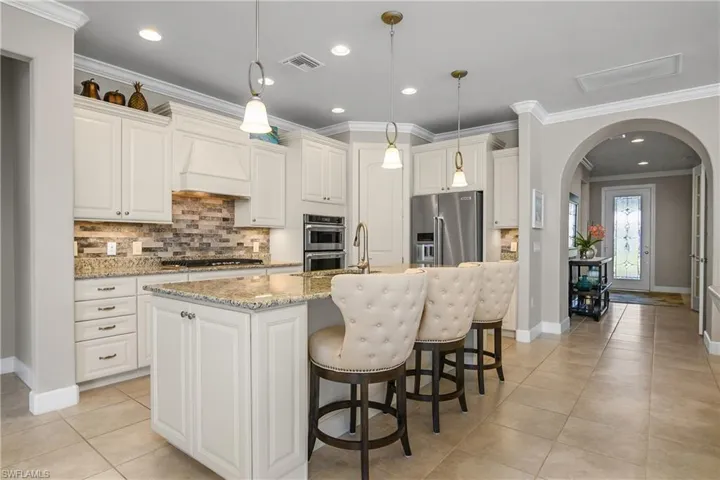 Kitchen featuring appliances with stainless steel finishes, decorative light fixtures, a kitchen island with sink, and custom range hood