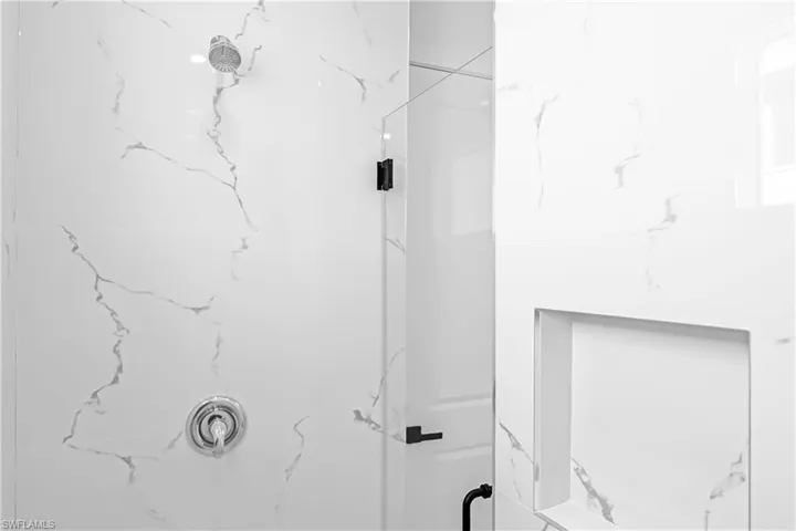 Shower with large format white tile featuring gray veining, a built-in niche, and a glass enclosure with matte black hardware