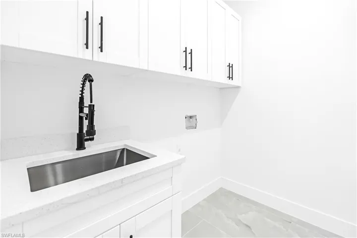 Utility sink with a matte black pull-down faucet, white upper and lower cabinetry with black hardware, white solid surface countertop, and light gray tile flooring