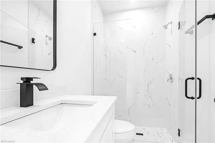 Contemporary bathroom featuring a frameless glass shower enclosure with matte black hardware, white marbled wall tiling, and a white vanity with an integrated sink and a matte black faucet