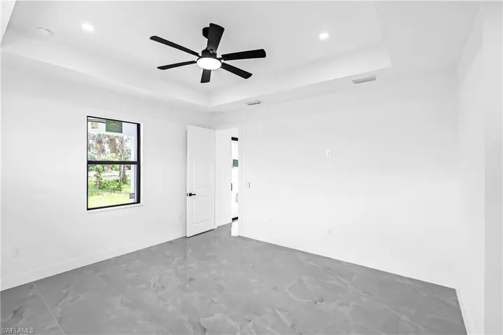 Spacious room featuring large format tile flooring, a tray ceiling with a modern ceiling fan, recessed lighting, and a single window with black trim