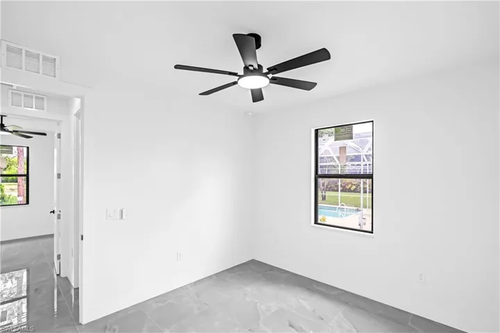 Bright interior space featuring a matte black ceiling fan with integrated lighting, large format tile flooring, and a window overlooking a screened pool area
